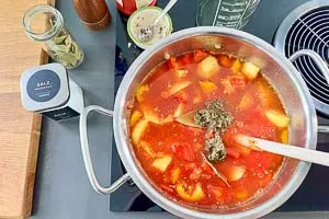 Kartoffeln, Paprika, passierte Tomaten, Gemüsebrühe, Lorbeerblätter, Pfeffer, Salz, Zucker und Gulaschgewürze vermengen und köcheln lassen.