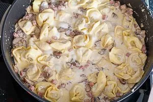 Parmesan und ungekochte Tortellini in die Soße rühren