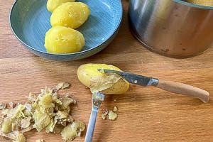 Mit Gabel und Messer die Kartoffeln pellen und die dunklen Stellen wegschneiden