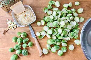 Rosenkohl waschen, äußere Blätter entfernen, Strunk abschneiden und halbieren. Knoblauch hacken und Parmesan reiben