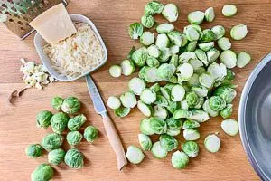 Rosenkohl waschen, äußere Blätter entfernen, Strunk abschneiden und halbieren. Knoblauch hacken und Parmesan reiben