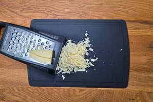 Bergkäse auf einer Küchenreibe grob reiben