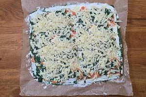 Geriebenen Bergkäse auf dem Spinat verstreuen