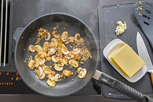 Butter, Zwiebeln und Champignons in einer Pfanne anrösten