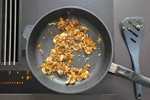 Eingeweichte Pilze und Knoblauchw&uuml;rfel in die Pfanne geben
