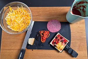 Teig auf der oberen Platte vorbacken, Tomatensoße, Parmesan, Salami, Spitzpaprika, schwarze Oliven und geriebenen Käse darauf verteilen.