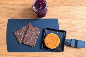 Backcamembert ins Pfännchen geben und danach mit Preiselbeermarmelade und Schwarzbrot garnieren.