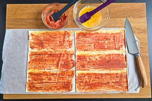 Rand des Blätterteigs mit Ei und Mitte mit der Würzsoße bestreichen