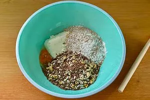 Haferflocken, Kleie, Quark, Eier, Gewürze, Backpulver, Natron, Samen, Kerne und Nüsse in eine Rührschüssel geben