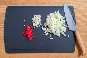 Zwiebeln, Knoblauch und Peperoni klein schneiden.