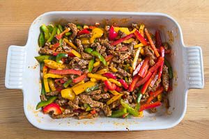 Paprikastreifen und Fleisch in eine Auflaufform geben.