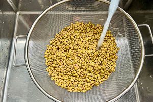 Eingeweichte Linsen in einem Sieb mit kaltem Wasser abspülen