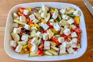 Geschnittene Oliven und Feta &uuml;ber dem Gem&uuml;se verteilen