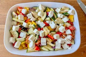 Geschnittene Oliven und Feta &uuml;ber dem Gem&uuml;se verteilen
