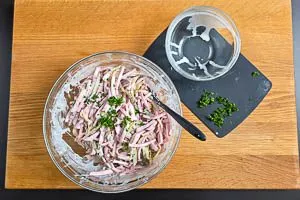 Dressing und die H&auml;lfte der Petersilie mit der Fleischwurst und den Gurken vermengen. Vor dem Servieren den Rest der Petersilie dar&uuml;berstreuen