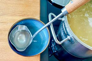 Nudelwasser mit einer Kelle abschöpfen