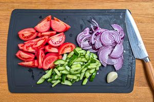 Rote Zwiebeln, Tomaten und Gurke schneiden. Knoblauchzehe sch&auml;len.