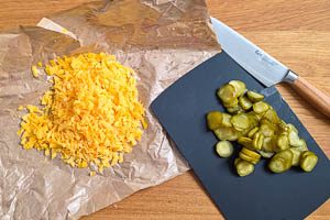 Cheddar reiben und Gew&uuml;rzgurken in Scheiben schneiden.