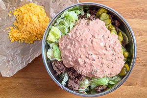 Hackfleisch und Gew&uuml;rzgurken zu dem Salat geben. So&szlig;e dar&uuml;bergie&szlig;en.