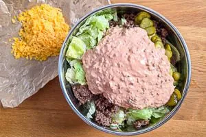 Hackfleisch und Gew&uuml;rzgurken zu dem Salat geben. So&szlig;e dar&uuml;bergie&szlig;en.