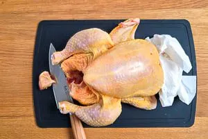 H&auml;hnchen abtupfen, B&uuml;rzel abschneiden, Fl&uuml;gel verschr&auml;nken und Fl&uuml;gelspitze &uuml;ber den Unterarm