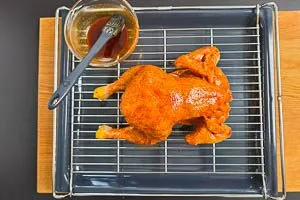 H&auml;hnchen auf ein Rost und darunter ein Backblech, mit Marinade bestreichen