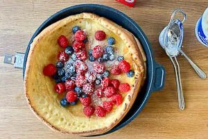 Ofenpfannkuchen mit Beeren belegen und Puderzucker bestreuen.