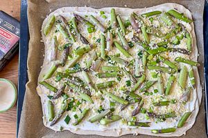 Spargel und Fr&uuml;hlingszwiebeln auf dem Teig verteilen, mit geriebenem Parmesan und Zitronenabrieb bestreuen