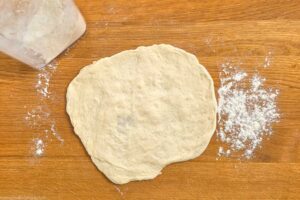 Teigkugeln auf einer bemehlten Arbeitsfl&auml;che zu Fladen formen