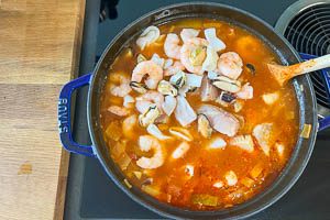 Nach der ersten Garzeit den Fisch und die Meeresfrüchte dazugeben, Lorbeerblätter und Sternanis entfernen, mit Salz, Cayennepfeffer und Orangenschale würzen