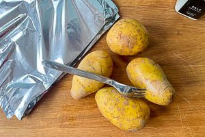 Mit einer Gabel L&ouml;cher in die Kartoffeln stechen, dann Alufolie zurechtschneiden