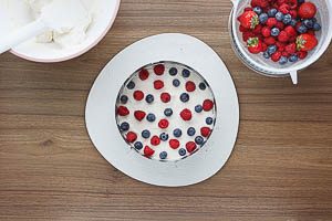 Sahne-Frischkäse-Creme und Beeren auf dem Biskuitboden verteilen