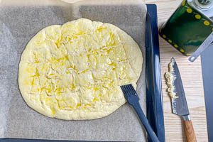 Mit einem Messer ein Rautenmuster in den Teig einritzen, Oliven&ouml;l darauf verstreichen und den Teig backen
