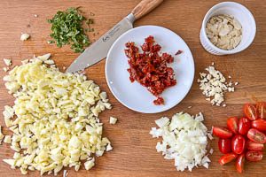 Getrocknete Tomaten, frische Tomaten, Zwiebeln, Zucchini-Fruchtfleisch und Knoblauch schneiden