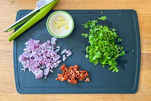 Zwiebel, Knoblauch, getrocknete Tomaten und Petersilie vorbereiten.