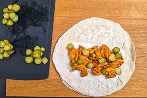 Gew&uuml;rzgurkenscheiben zum Fleisch auf den Wrap geben