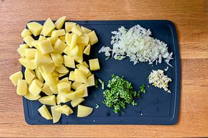Kartoffeln sch&auml;len, w&uuml;rfeln sowie Zwiebel, Knoblauch und Petersilie kleinschneiden