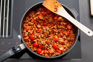 Knoblauch, Tomatenmark und Kirschtomaten in die Pfanne geben.