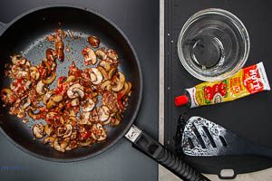 Zwiebeln, Knoblauch und Speck zu den Champignons geben und mit Tomatenmark anbraten
