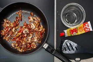 Zwiebeln, Knoblauch und Speck zu den Champignons geben und mit Tomatenmark anbraten