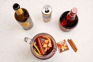Alle restlichen Zutaten in die Karaffe geben: Pfirsiche, Zimtstangen, Rotwein, Orangenlikör und Zitronenlimonade.