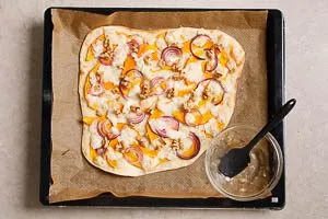 K&uuml;rbis-Flammkuchen nach dem Backen mit Honig betr&auml;ufeln und mit N&uuml;ssen belegen