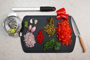 Limette abwaschen, Schale abreiben und Saft auspressen, Knoblauch, Schalotten, Gew&uuml;rzgurken, Paprika und Peperoni w&uuml;rfeln, Koriander waschen und hacken