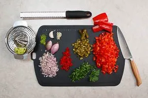 Limette abwaschen, Schale abreiben und Saft auspressen, Knoblauch, Schalotten, Gewürzgurken, Paprika und Peperoni würfeln, Koriander waschen und hacken