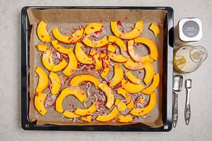 K&uuml;rbisspalten, Zwiebelhalbringe und gew&uuml;rfelte Peperoni auf einem Backblech