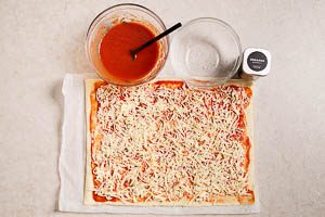 Pizzateig ausrollen, mit Pizzaso&szlig;e bestreichen, mit K&auml;se und Oregano bestreuen